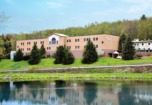 A serene view of a multi-story building alongside a calm body of water, surrounded by lush greenery.