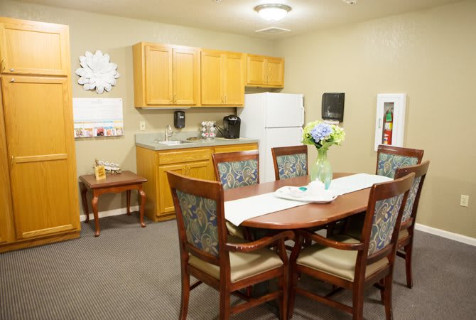 A cozy kitchen and dining area with a wooden table, cushioned chairs, and a flower vase centerpiece.