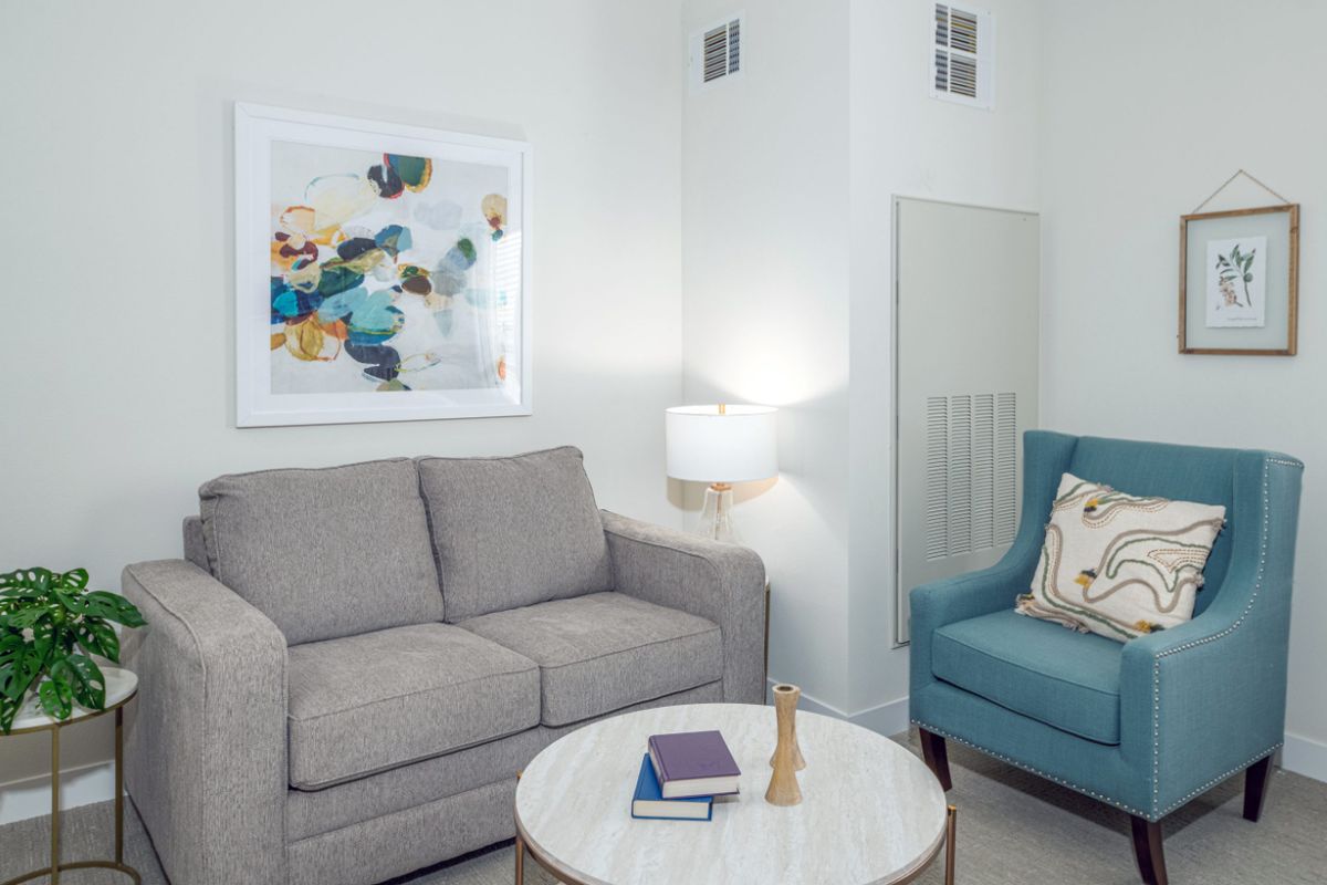 A cozy living room with a gray sofa, blue armchair, and a stylish lamp beside a round coffee table.