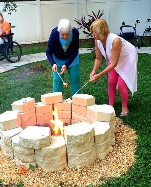 Two people roasting marshmallows over a fire pit in a garden.