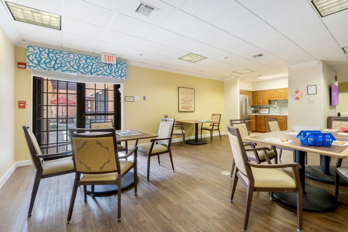A spacious and bright dining area with several tables and chairs, adjacent to a kitchen.