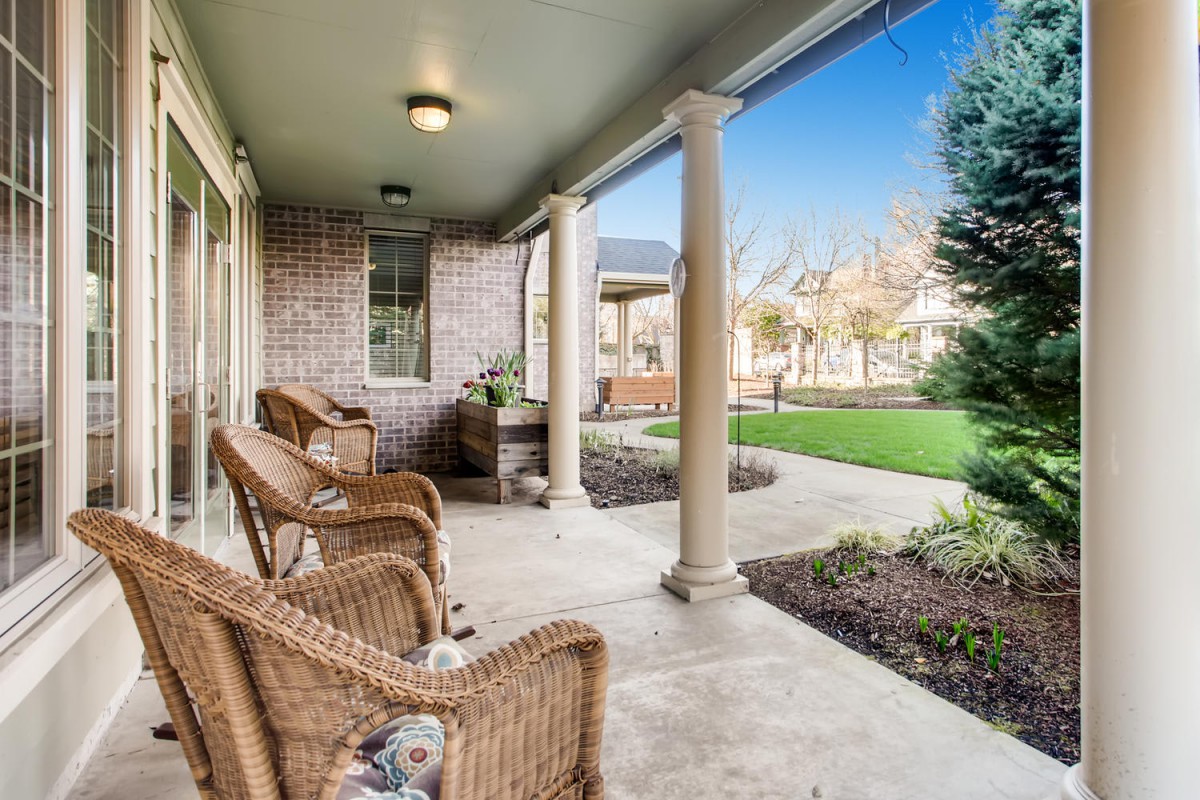 A covered porch with wicker chairs and columns overlooks a landscaped front yard.