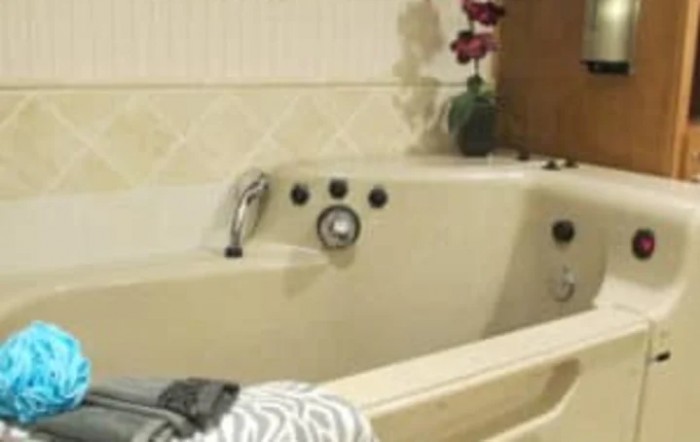 A cozy bathroom featuring a cream-colored bathtub with a nearby folded towel and decorative flowers.