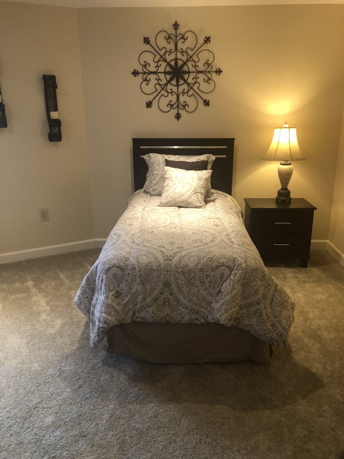 A cozy bedroom with a single bed, nightstand, and warm lighting.