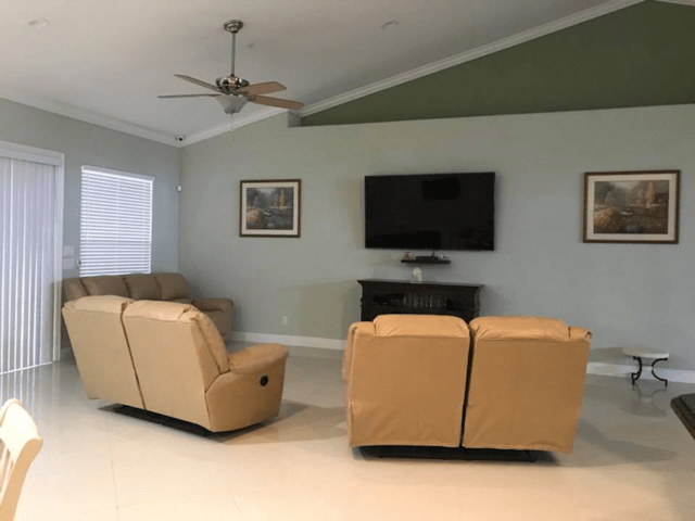 A cozy living room with tan couches facing a wall-mounted television flanked by framed art.
