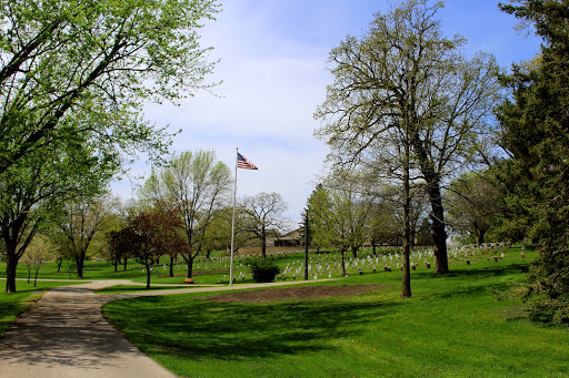 A serene park scene featuring a flag, lush green grass, and trees under a clear blue sky.