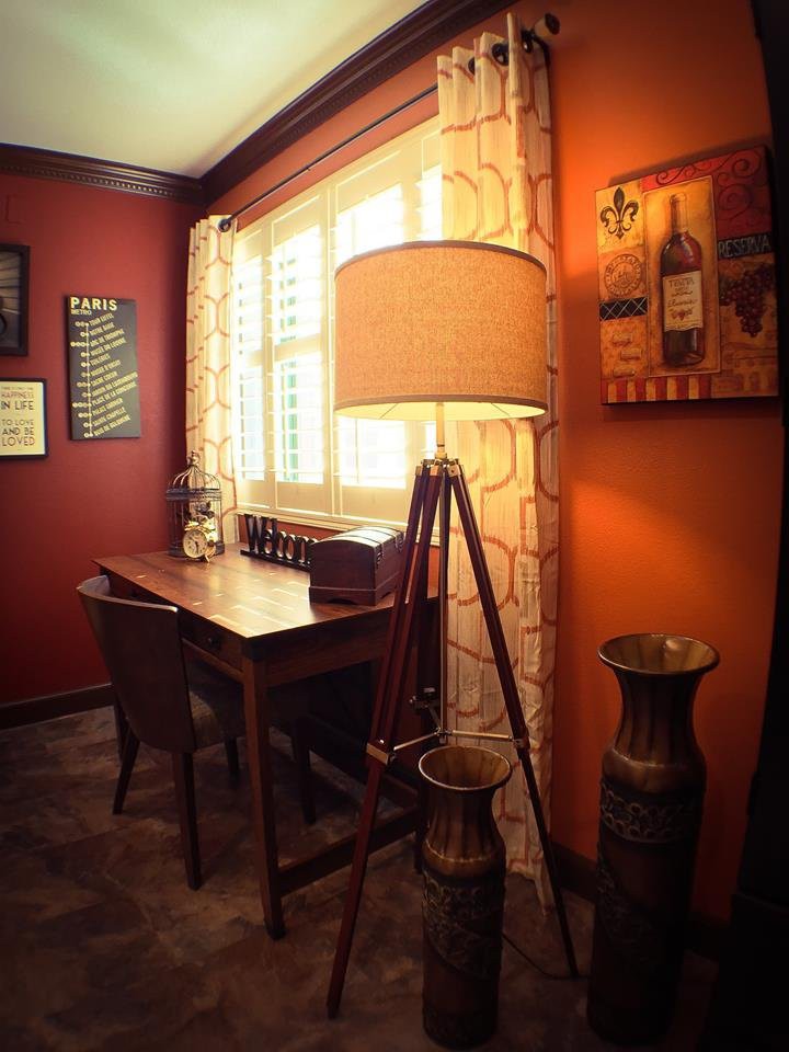 A cozy home office with vintage decor, featuring a wooden desk and a tripod lamp in warm hues.