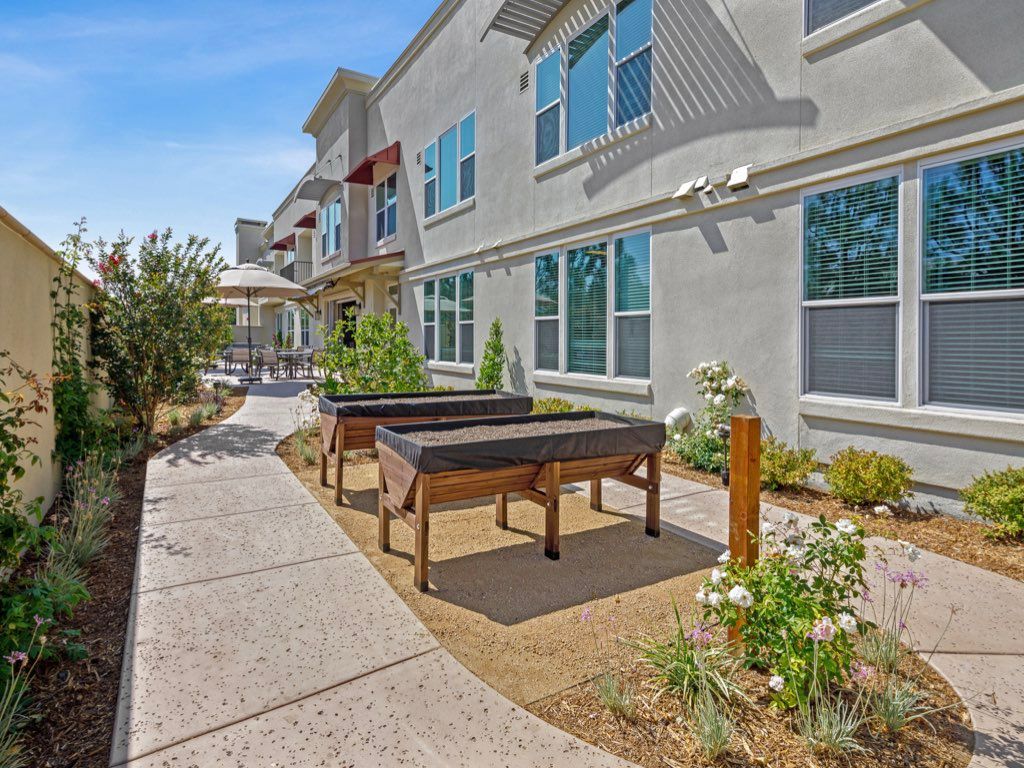 A sunny outdoor area featuring a walkway, foosball tables, and landscaped garden beside a modern building.