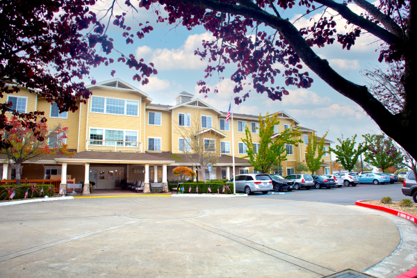 A multi-story building with a parking lot and trees, seen on a clear day.