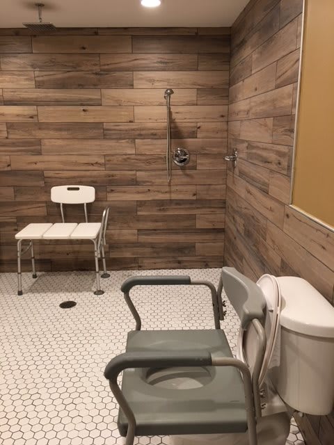 An accessible bathroom with a tiled floor and wooden wall panels, featuring a shower area and chairs for assistance.