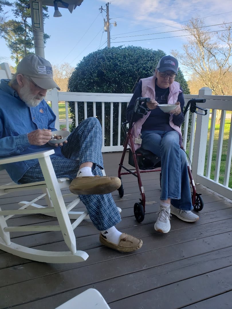 An elderly couple sits leisurely on a porch, enjoying a peaceful moment together.