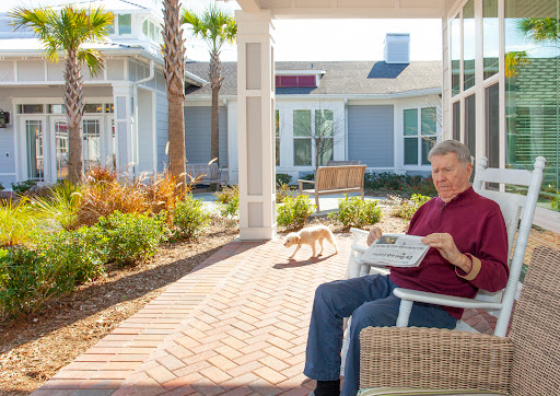 A senior citizen enjoying a relaxing day outdoors, reading a newspaper while their pet dog strolls nearby.