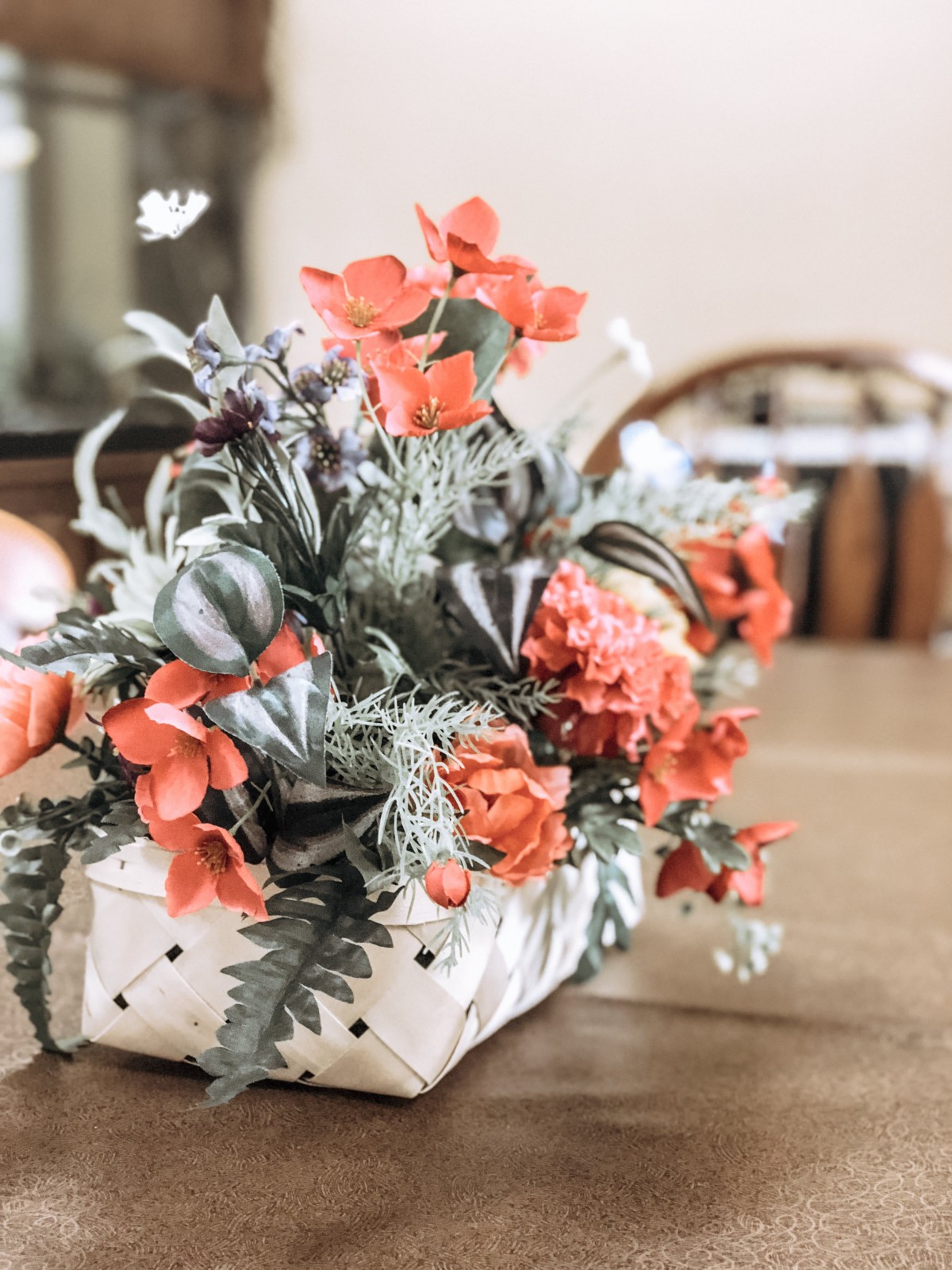 A vibrant floral arrangement with orange flowers in a woven basket sits on a wooden table.