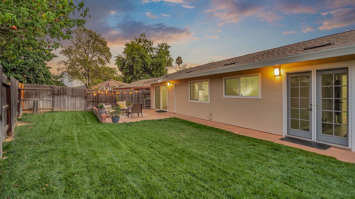 A serene backyard with a well-maintained lawn, cozy patio seating, and a beautiful sunset backdrop.