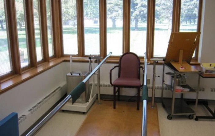 A physical therapy room with parallel bars and a chair for rehabilitation exercises.