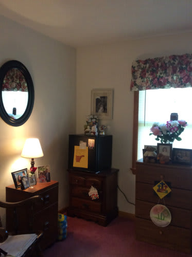 Cozy bedroom corner with a lamp, mirror, dresser, and television.