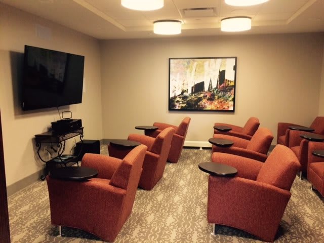 A cozy lounge area with orange chairs facing a large television.
