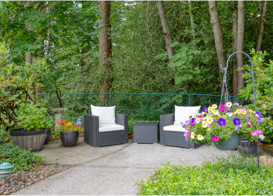 A cozy patio setup with two chairs and vibrant flower arrangements surrounded by lush greenery.