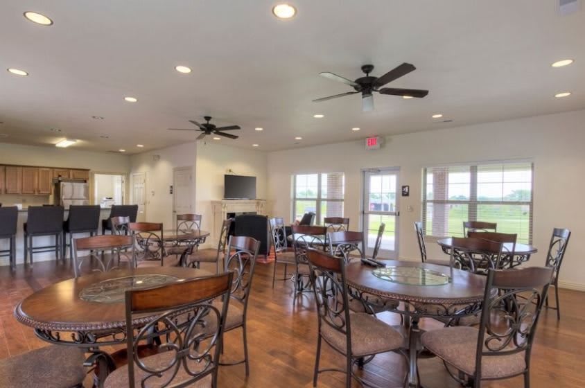 A spacious indoor dining area with multiple tables and chairs, ceiling fans, and large windows.