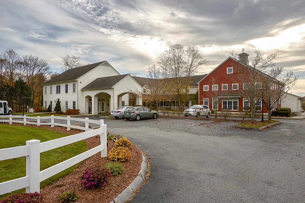 A scenic view of a white building and red barn with a parking area in front.