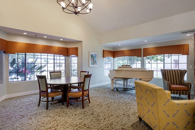 A spacious living room featuring a dining area, large windows, and a grand piano.