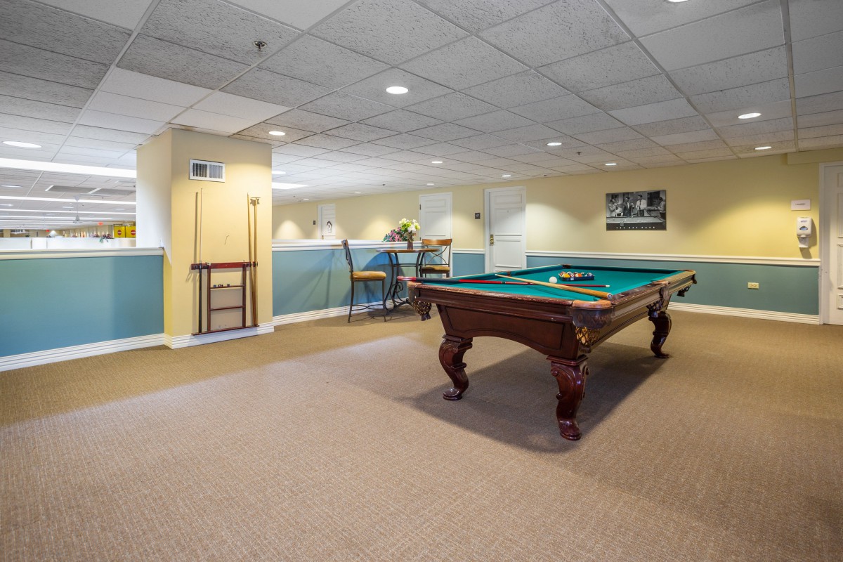 A spacious game room featuring a pool table with warm lighting.
