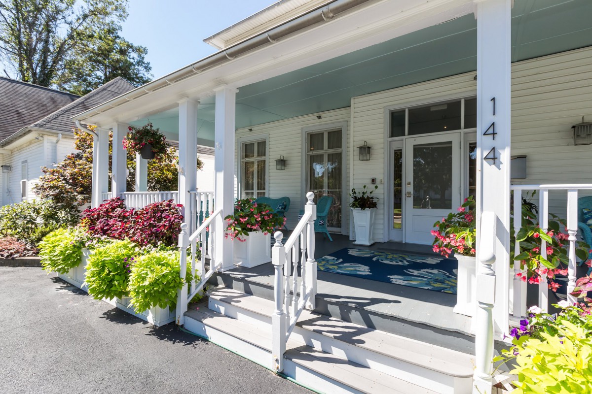 A charming porch with white columns and steps, adorned with vibrant flowers and outdoor seating.