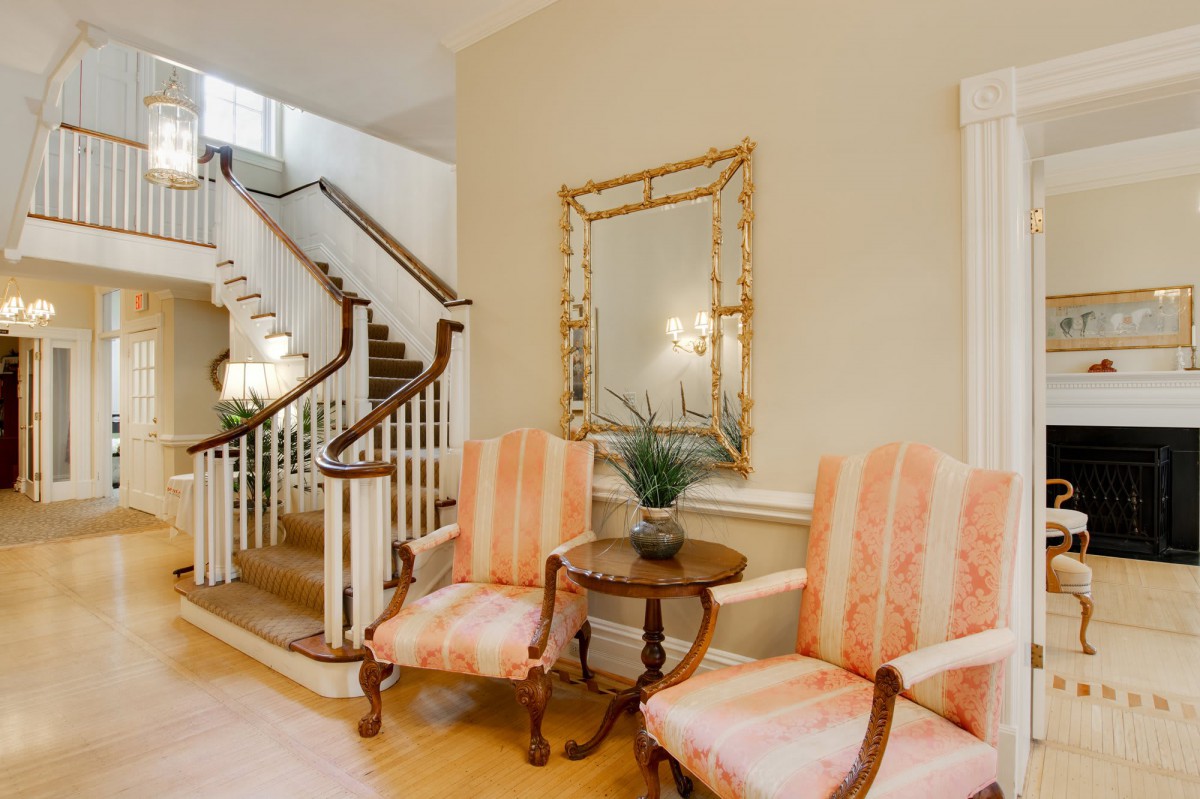 A cozy hallway with elegant chairs, a wooden table, and a decorative mirror beside a staircase.