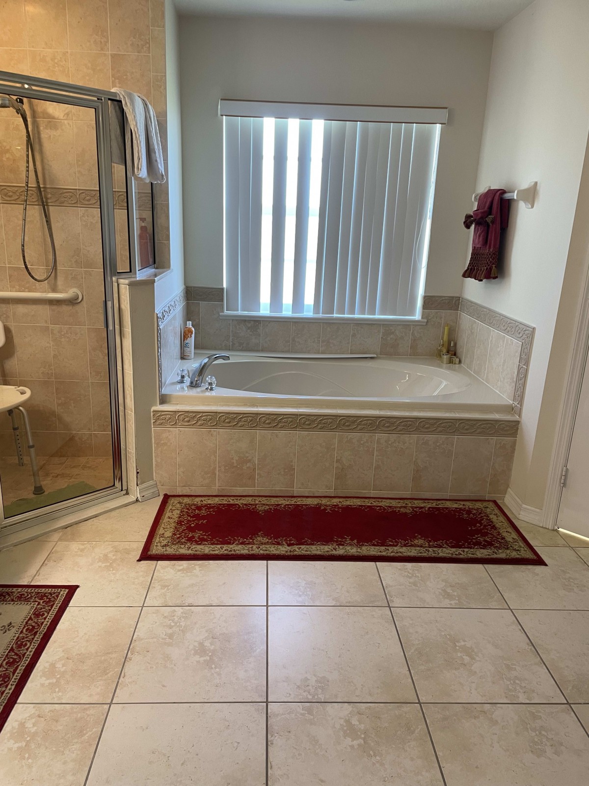 A bathroom with a shower, bathtub, and red rugs on a tile floor.