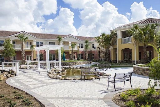 A beautiful courtyard featuring a serene water pond and comfortable benches, surrounded by residential buildings under a partly cloudy sky.