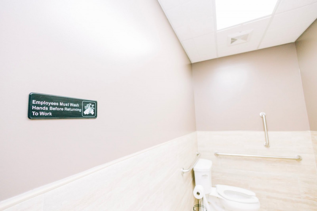 A clean public restroom with a toilet and a sign on the wall.