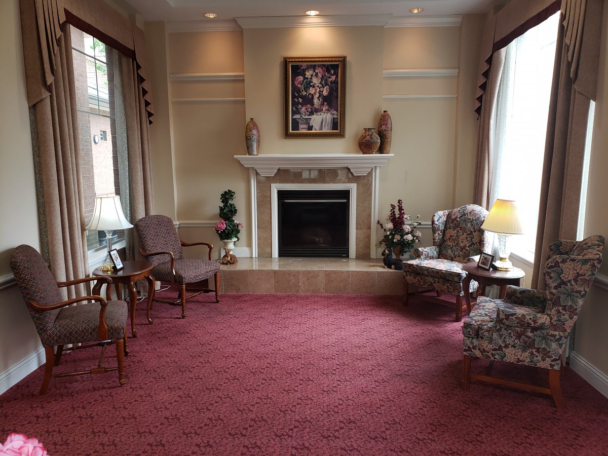 A cozy living room featuring a central fireplace, surrounded by armchairs and adorned with decorative elements.