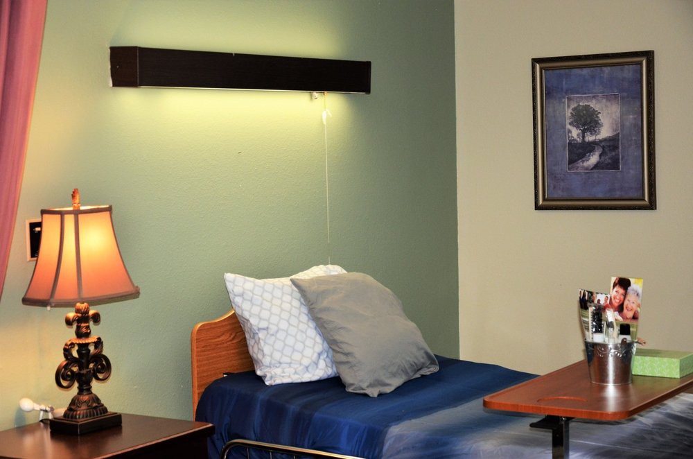 A neatly arranged bedroom with a single bed, pillows, lighting fixtures, and a painting on the wall.