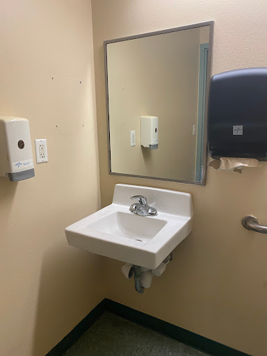 A clean bathroom setting featuring a sink, mirror, and hygiene dispensers.