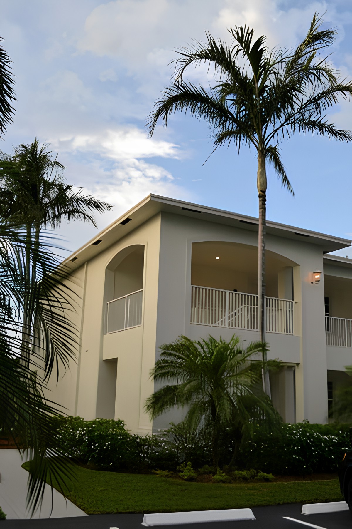 A tropical-style house with a balcony surrounded by palm trees.
