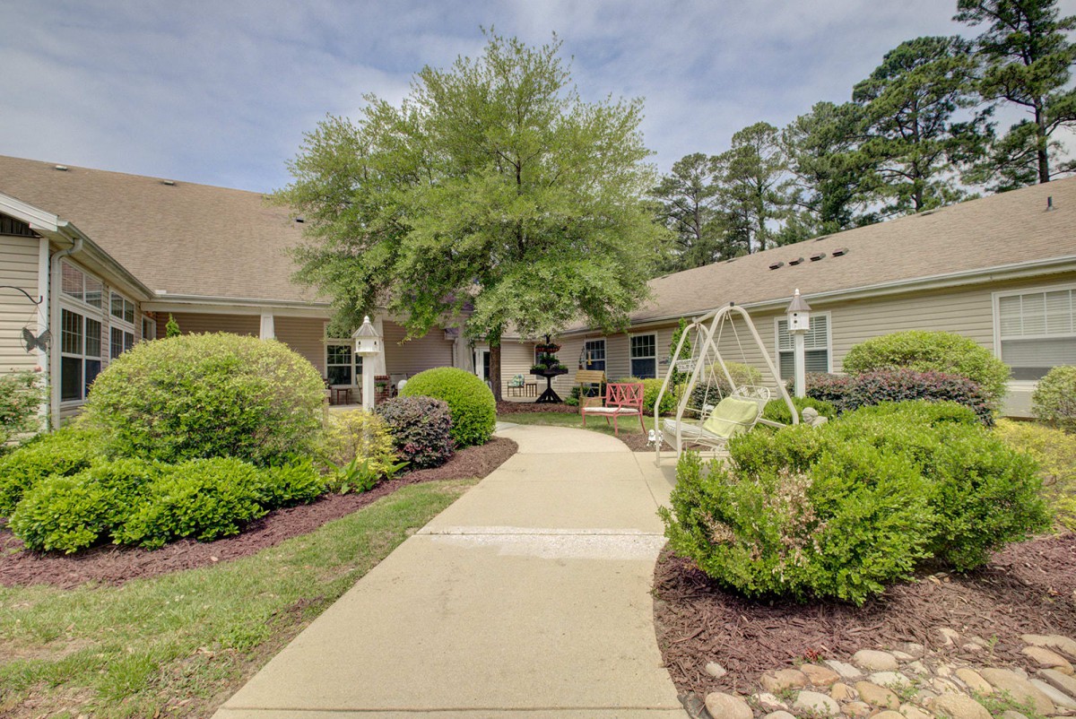 A serene courtyard with a pathway leading through lush gardens and a swing set near a building.