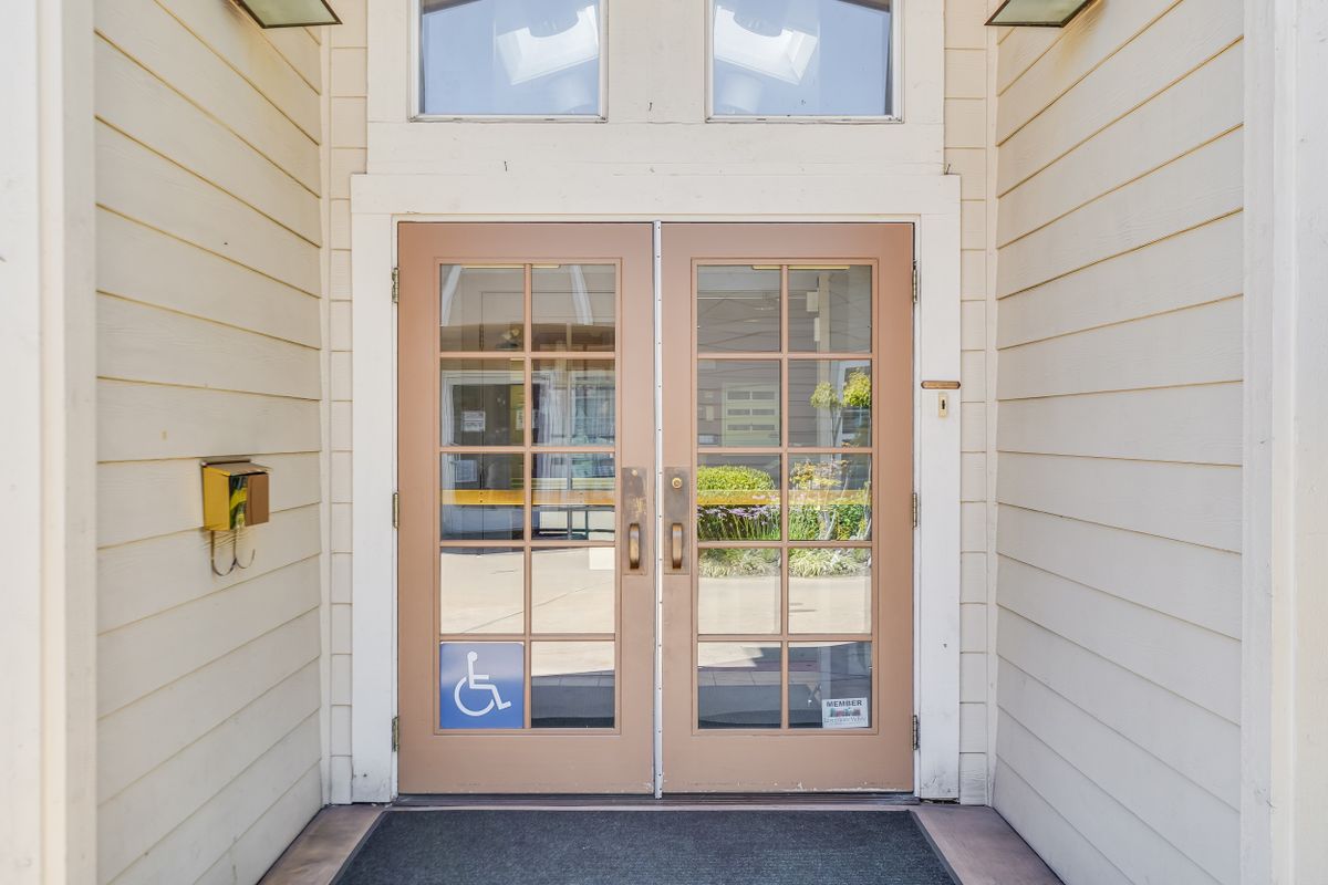 Glass double doors serving as the entrance to a building, featuring accessibility signage.