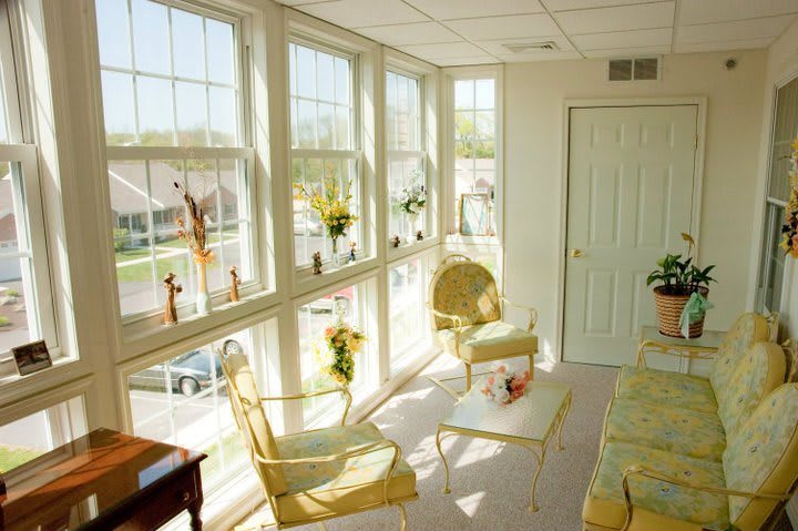 A bright sunroom featuring large windows, elegant chairs, and a small table adorned with decorative items.