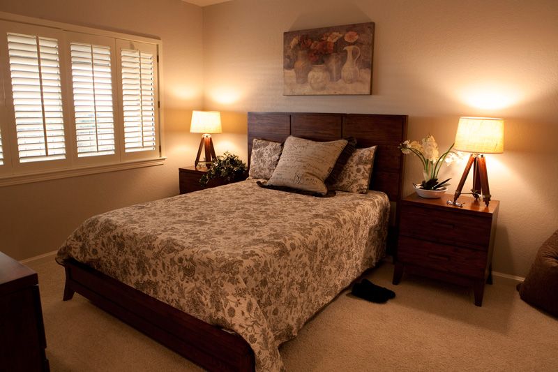 A cozy bedroom with warm lighting, featuring a bed with patterned bedding, two lamps on nightstands, and artwork above the headboard.