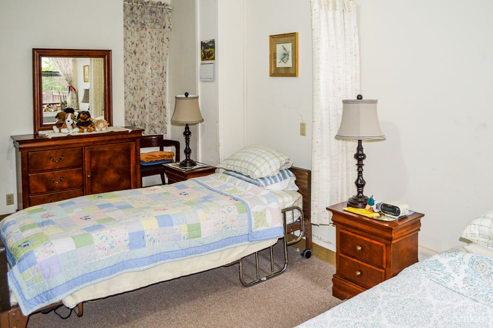 A cozy bedroom with twin beds featuring quilted bedding, accompanied by nightstands and lamps. A mirror and additional decor complete the space.