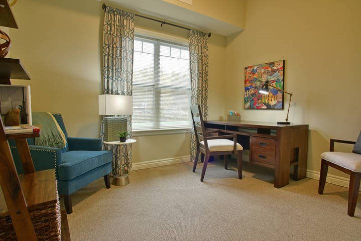 A cozy home office with a wooden desk, chair, and a comfortable armchair by the window.