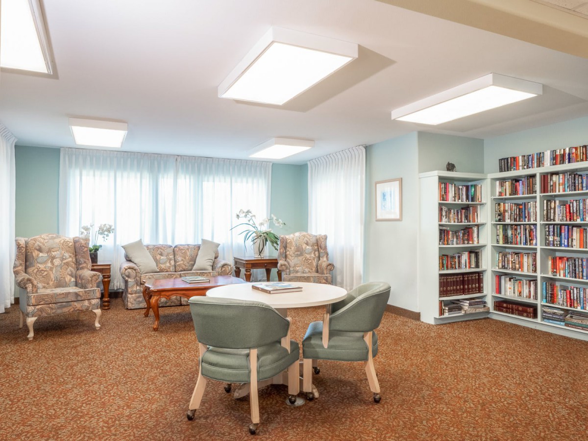 A cozy living room with a small library, featuring comfortable seating, a central table, and bookshelves.