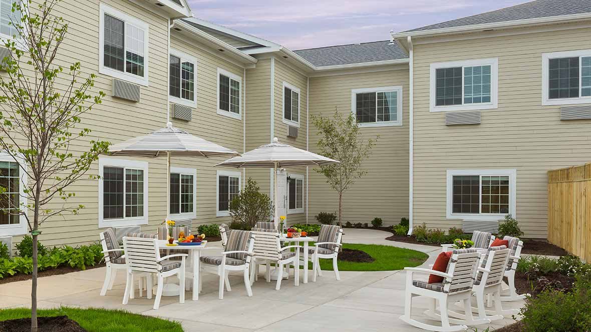 A cozy courtyard with outdoor seating and umbrellas, surrounded by a two-story building.
