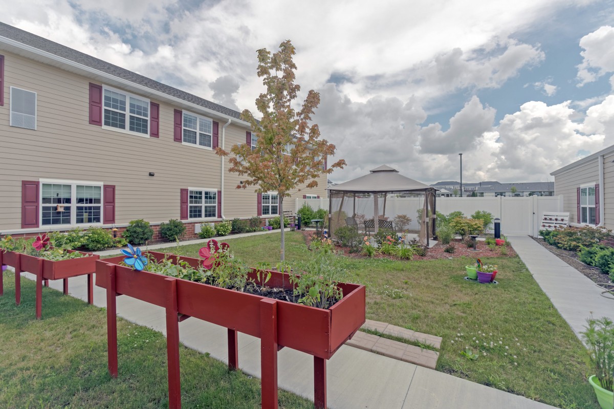 A community garden with raised planter boxes and a gazebo in an outdoor area beside a building.