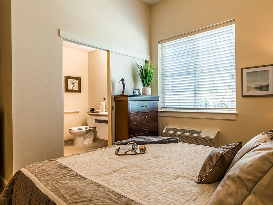 A cozy bedroom with a large window, featuring warm decor and an adjacent bathroom.