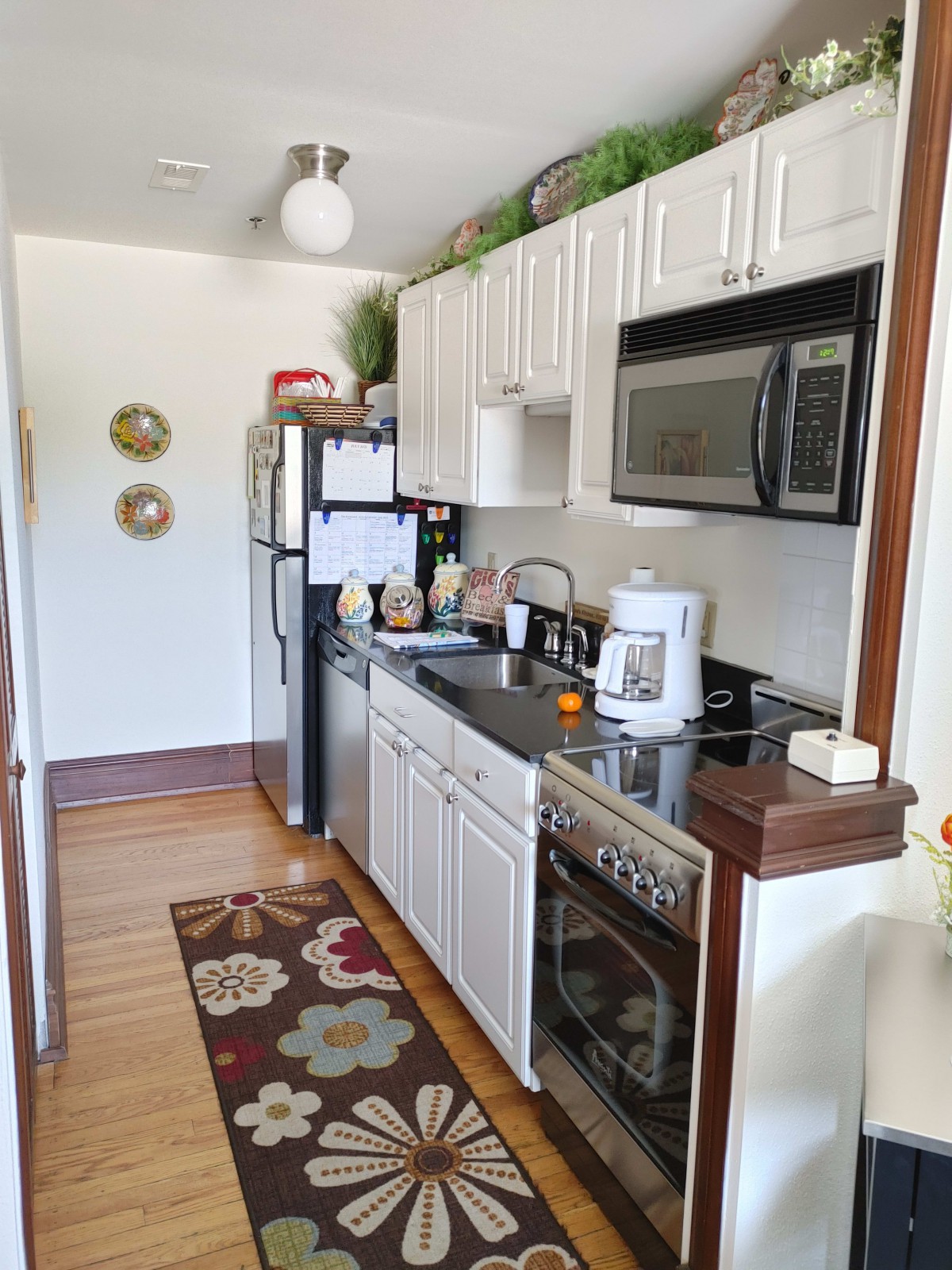 A compact kitchen with white cabinets, featuring a microwave, stove, and refrigerator.