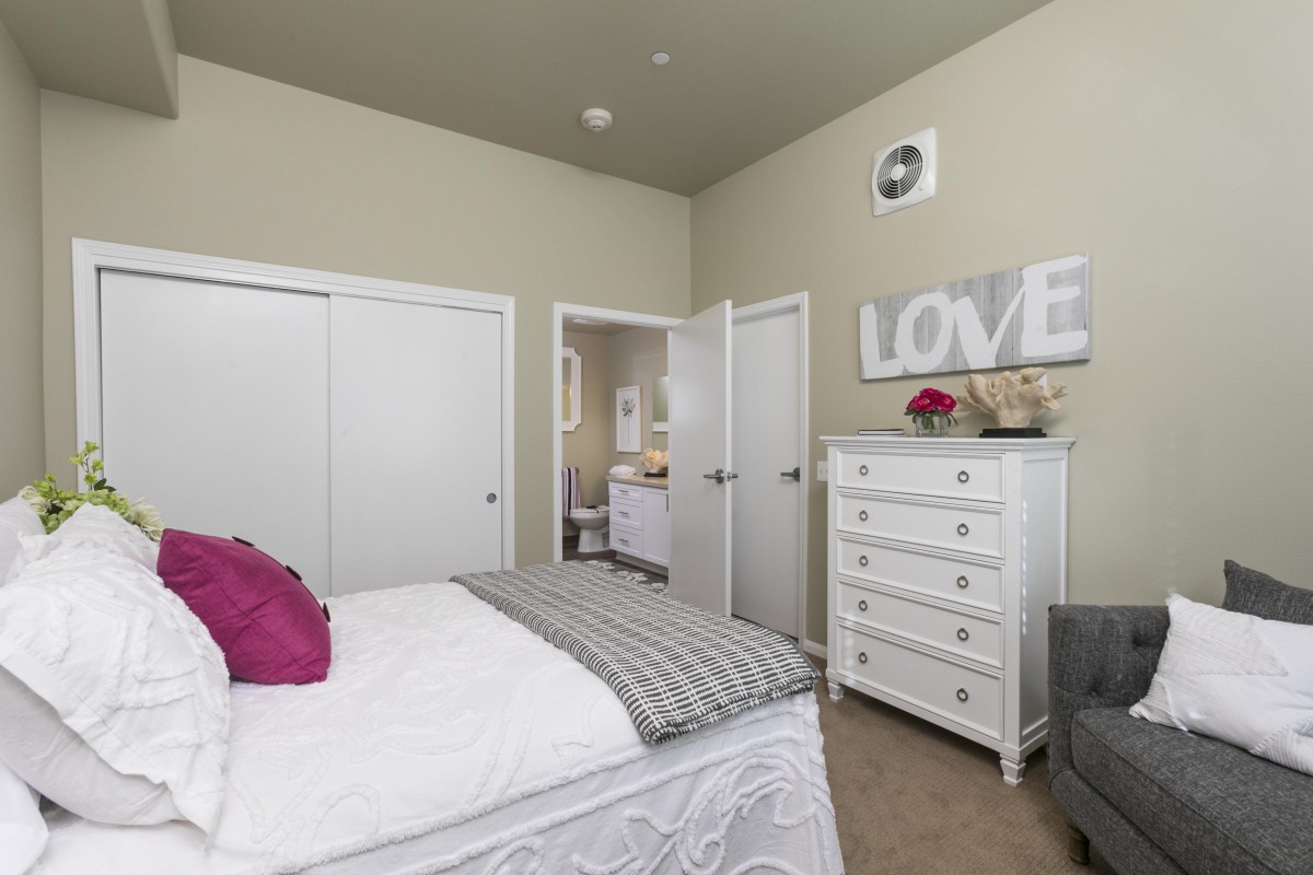 A cozy bedroom with a neatly made bed and a white dresser.