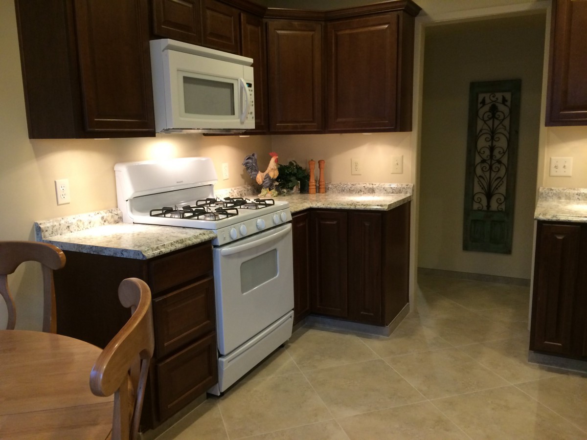 A cozy kitchen featuring dark wood cabinets, a microwave, and a gas stove.