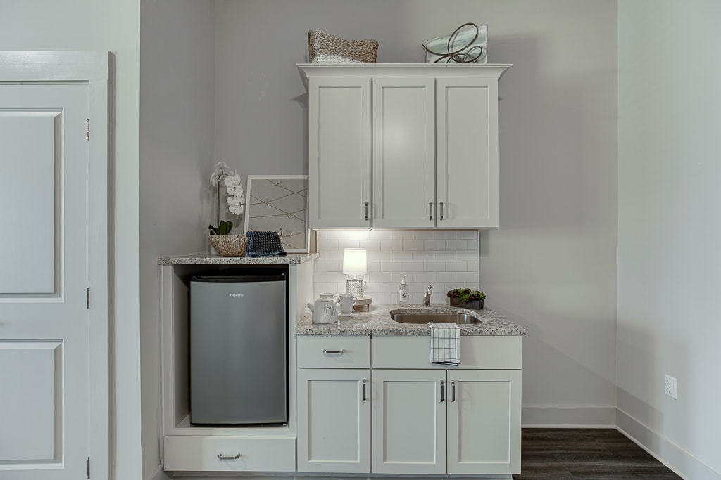 A compact kitchenette with white cabinets, a mini fridge, and decorative items.
