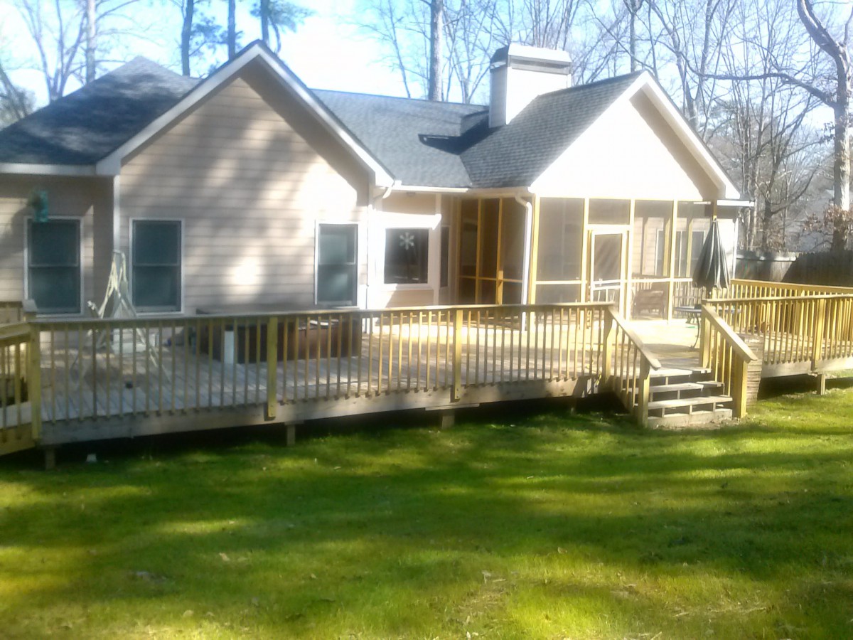 A cozy house with a wooden deck and a grassy yard on a sunny day.